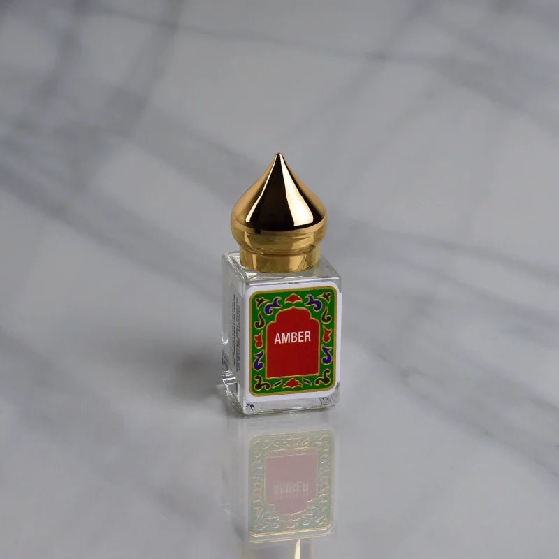 The Amber Perfume Oil by Nemat features a small glass bottle with a pointed gold cap and "Amber" label, shown on gray marble, ready to become your signature scent.