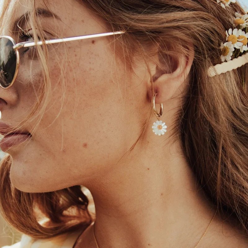 Close-up of a woman in sunglasses and a gold necklace, wearing Larissa Loden Barrymore Earrings and daisies tucked in her wavy hair.