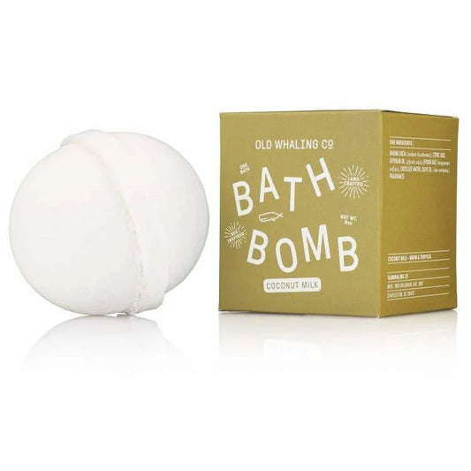 A white bath bomb rests beside a yellow-green box labeled "Bath Bomb | Coconut Milk | Old Whaling Co." by Old Whaling Co., ideal for a soothing soak.