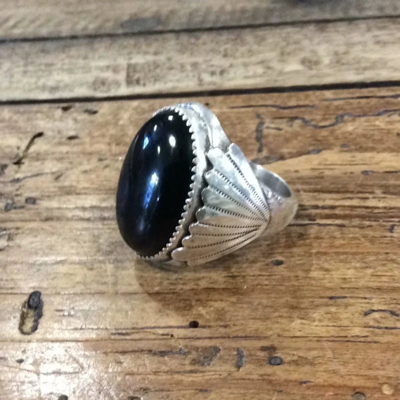 The Vintage Black Onyx Oval Ring features a striking oval black onyx stone in a decorative sterling silver bezel, shown on wood. Size 11.5.