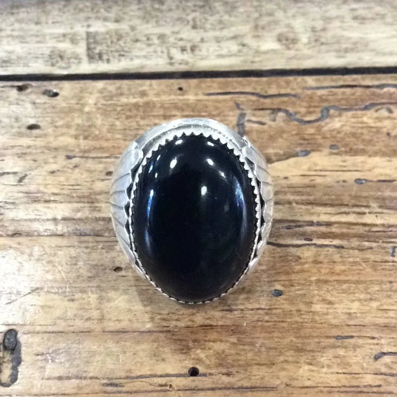 The Vintage Black Onyx Oval Ring in size 11.5 features a large black onyx stone set in sterling silver and is displayed on a rustic wooden surface.