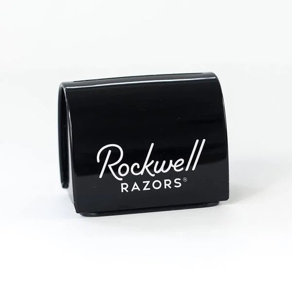 The Blade Bank by Rockwell Razors is a black blade storage container for used double-edge razor blades, featuring white branding on the front and shown against a plain white background.