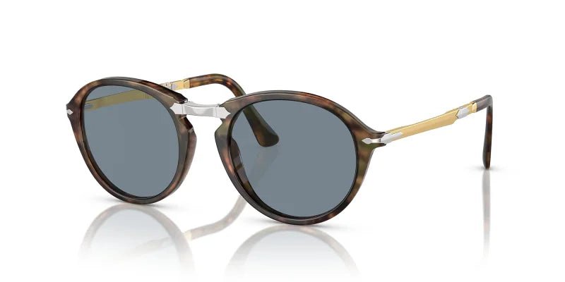 Persol Caffe w/ Light Blue 0PO3274S sunglasses feature a round acetate and metal frame, dark lenses, a sleek metal nose bridge, and gold arm accents, shown on a white background.