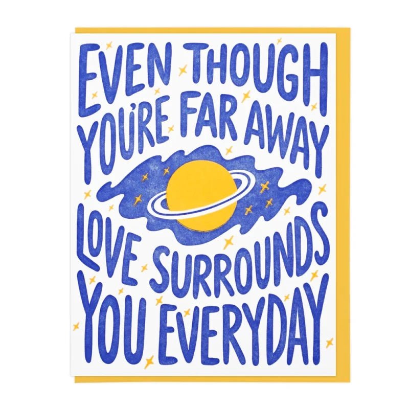The "Love Surrounds You" card by Lucky Horse Press features a yellow planet and stars, is letterpress printed, blank inside, and reads "Even though you're far away love surrounds you everyday" in bold blue letters.