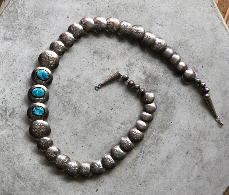 The Vintage Flat Concho Shadowbox Turquoise Necklace features three Kingman turquoise stones set in silver with elegant silver beads, beautifully displayed on a gray textured surface.