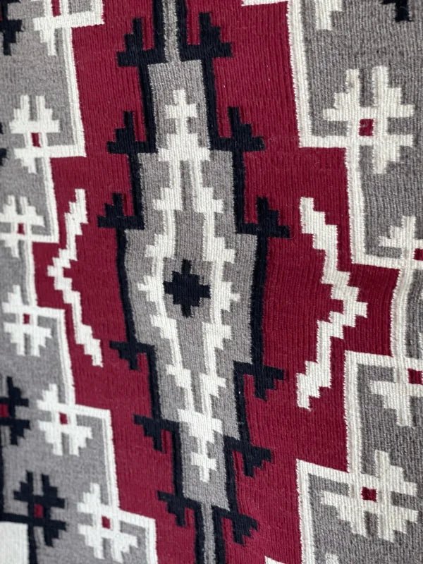 A close-up of the Ganado Rug Classic "Snowflake" CA 1980 by Vintage, showcasing woven red, gray, black, and white snowflake designs in a style reminiscent of Navajo weaving.