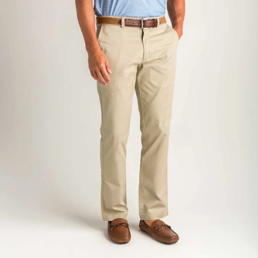 A person wearing Duck Head Gold School Chino pants, paired with a brown belt, brown loafers, and a light blue shirt, stands with hands in pockets against a plain background.