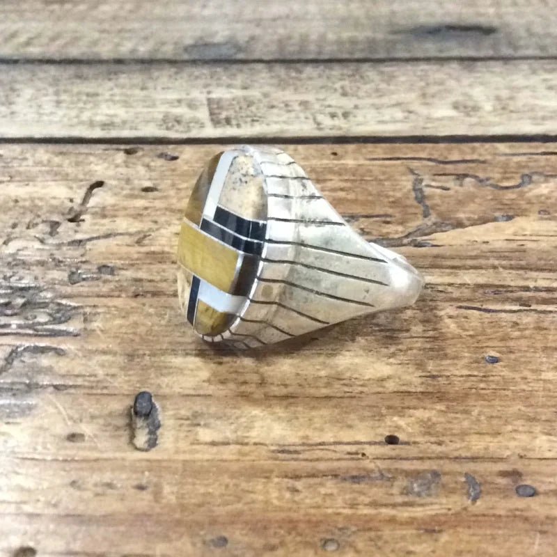 The Vintage Inlay Multi-stone Tiger's Eye Navajo Ring features a geometric design with gold, white, and black segments, inspired by Navajo artistry and displayed on rustic wood.