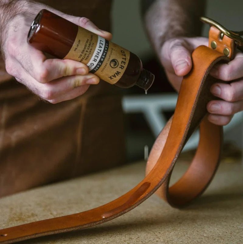 Using both hands, a person applies Otter Wax Leather Polishing Oil to a brown leather strap for all-natural care with Otter Wax’s signature bottle.