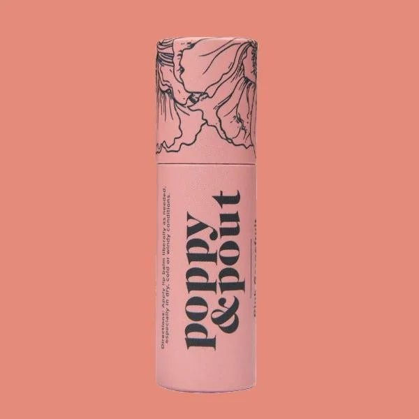 A pink cylindrical Poppy & Pout Lip Balm container with floral lid illustrations is shown against a solid pink background, emphasizing this handmade, cruelty-free natural lip balm by Poppy & Pout.
