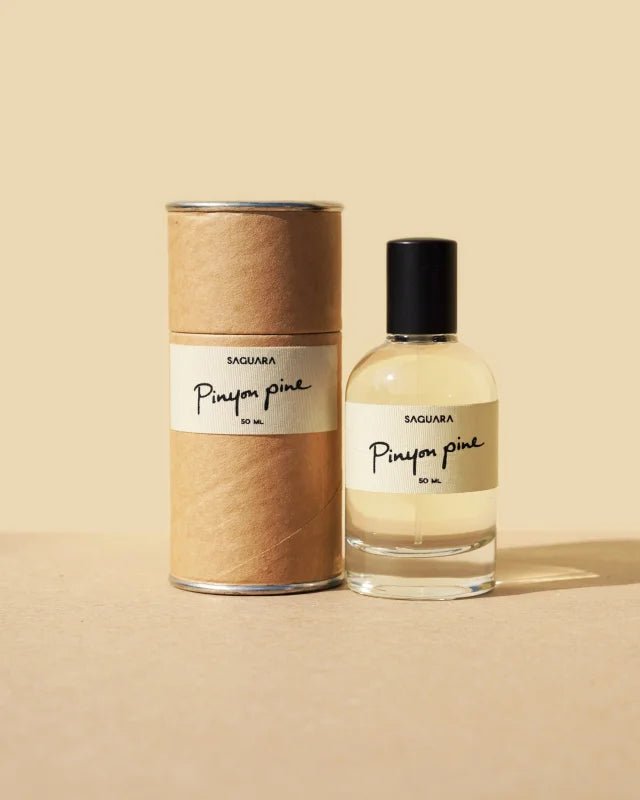 A bottle of Pinyon Pine by Saguara Perfumes rests beside its cylindrical box against a beige background.