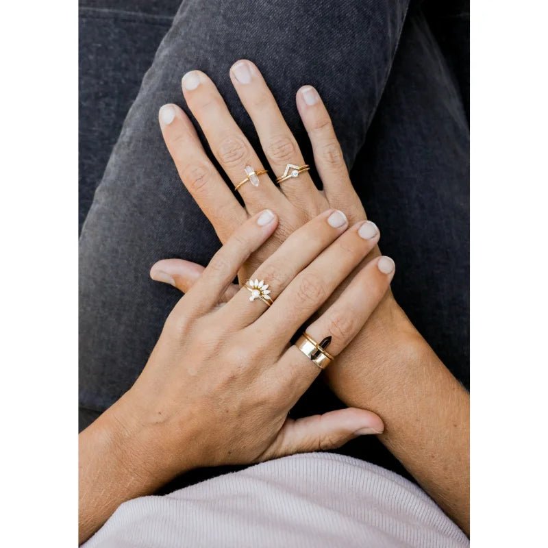 A person with light skin wears multiple hand-crafted gold rings, including the JaxKelly Ring | Smokey Quartz Point, resting their hands on their lap over dark pants.