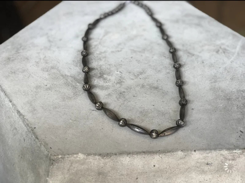 The Skinny Navajo Pearls | Vintage necklace by Vintage features a dark metal, lightweight design with alternating oval and round beads, inspired by classic Navajo Pearls—ideal for layering, shown on a light gray concrete block.
