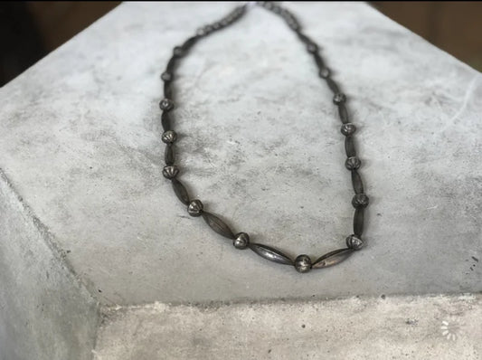The Skinny Navajo Pearls | Vintage necklace by Vintage features a dark metal, lightweight design with alternating oval and round beads, inspired by classic Navajo Pearls—ideal for layering, shown on a light gray concrete block.