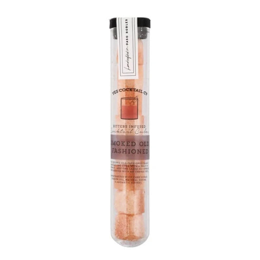 A clear plastic tube contains Yes Cocktail Co.'s Smoked Old Fashioned Cocktail Cubes—pink organic cane sugar cubes, ideal for crafting smoked old fashioned cocktails with bitters.