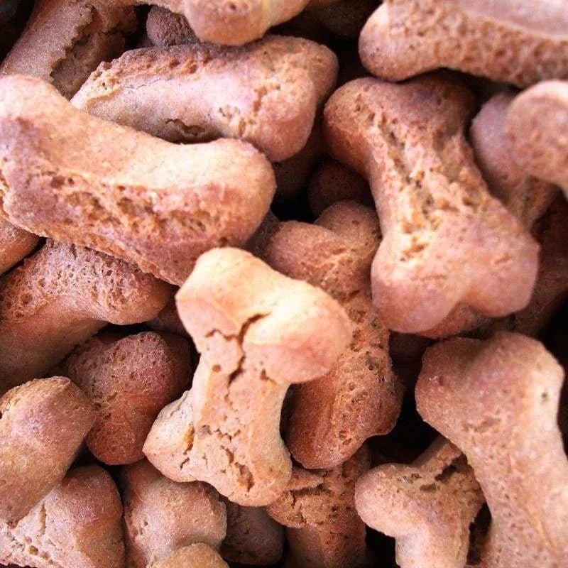 A close-up of several Tiny Bones dog treats by Urban Dog Barkery, shaped like bones and stacked together.