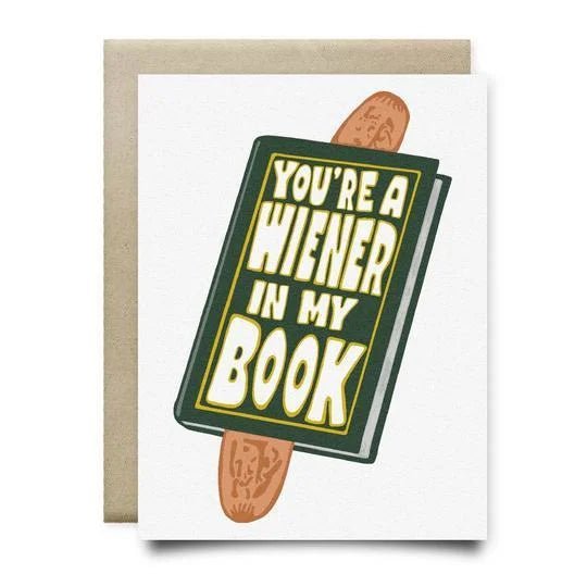 The "You're A Wiener In My Book Card" by Anvil Cards is an A2 greeting card with a blank inside, featuring a book and hot dog illustration and the phrase "You're a Wiener in My Book" on the cover.