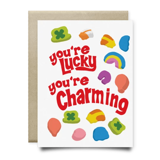 The "You're Lucky You're Charming Card" by Anvil Cards features red lettering surrounded by marshmallow shapes inspired by Lucky Charms, printed on quality linen paper. A2 size, blank inside for your message.