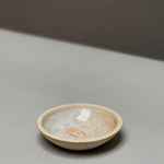The Stoneware Holder | Incausa by Incausa is a small, shallow hand-thrown incense burner with a light beige and speckled glaze, displayed on a smooth, light gray surface.