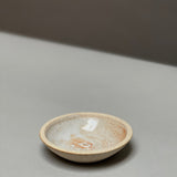 The Stoneware Holder | Incausa by Incausa is a small, shallow hand-thrown incense burner with a light beige and speckled glaze, displayed on a smooth, light gray surface.