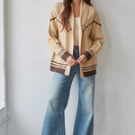 A woman stands against a wall wearing the By Together Knit Sweater Cardigan Top with star and horse jacquard detail, paired with a cream top and high-waisted wide-leg jeans.