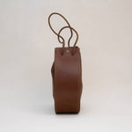 Side view of the Stash Joi Bag in Chestnut Distressed leather, featuring a visible seam, snap button closure, and an adjustable shoulder strap against a plain background.