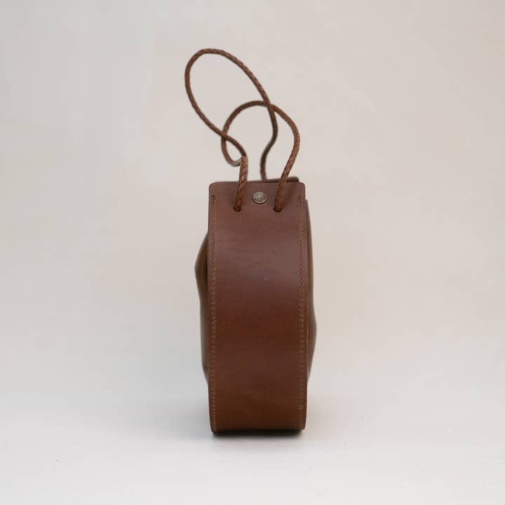 Side view of the Stash Joi Bag in Chestnut Distressed leather, featuring a visible seam, snap button closure, and an adjustable shoulder strap against a plain background.