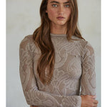 A woman with long brown hair stands with her arms crossed, facing the camera against a neutral background, wearing the By Together Knit Seamless Jacquard Mock Neck Long Sleeve Top and blue jeans.