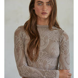 A woman with long brown hair stands with her arms crossed, facing the camera against a neutral background, wearing the By Together Knit Seamless Jacquard Mock Neck Long Sleeve Top and blue jeans.