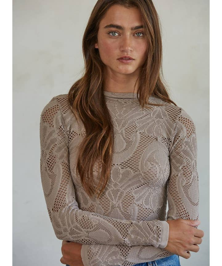 A woman with long brown hair stands with her arms crossed, facing the camera against a neutral background, wearing the By Together Knit Seamless Jacquard Mock Neck Long Sleeve Top and blue jeans.
