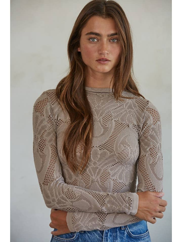 A woman with long brown hair stands with her arms crossed, facing the camera against a neutral background, wearing the By Together Knit Seamless Jacquard Mock Neck Long Sleeve Top and blue jeans.