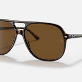 The Ray-Ban Bill RB2198 sunglasses, presented in a classic tortoiseshell aviator design with brown polarized lenses and signature Ray-Ban logos on both the lenses and arms, are elegantly displayed against a simple light backdrop.