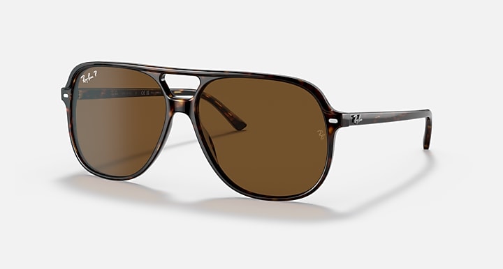 The Ray-Ban Bill RB2198 sunglasses, presented in a classic tortoiseshell aviator design with brown polarized lenses and signature Ray-Ban logos on both the lenses and arms, are elegantly displayed against a simple light backdrop.