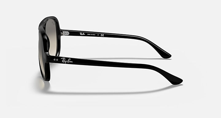 The Ray-Ban RB4125 sunglasses are featured from a side angle, highlighting the iconic brand logo on both the temple and inside arm. These sunglasses showcase a polished black frame with light grey gradient lenses, set against a plain white background for a modern look.