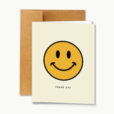 Thank You | Notecard by Ramble & Company features a large yellow smiley face in the center with the words “thank you” printed below. Presented with a brown envelope, this blank inside card is perfect for adding your own heartfelt message.