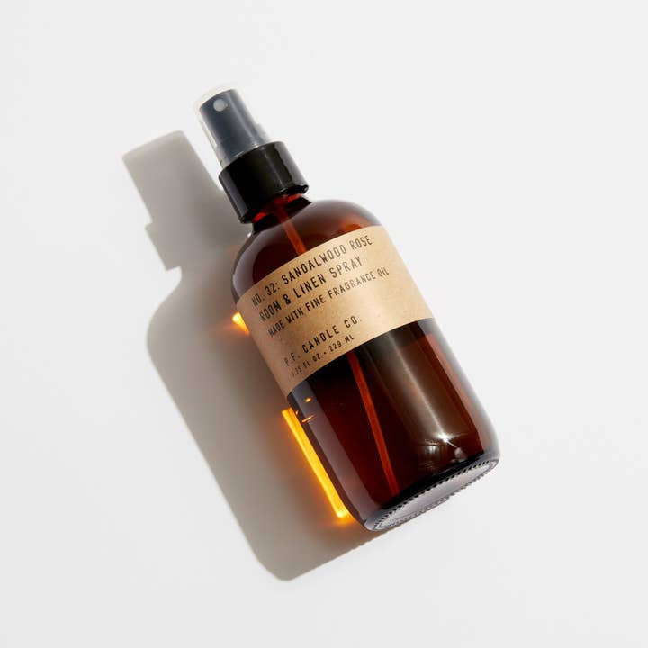 A brown glass spray bottle labeled "N0.32 Sandalwood Rose Room & Linen Spray" by P.F Candle, featuring a black nozzle and pictured on a white background, offers a soothing floral scent of cashmere rose.
