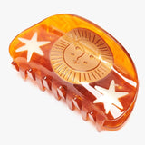 Hemera Claw by Winona Irene: an amber-colored acetate hair claw clip featuring a gold sun face emblem and white star accents.