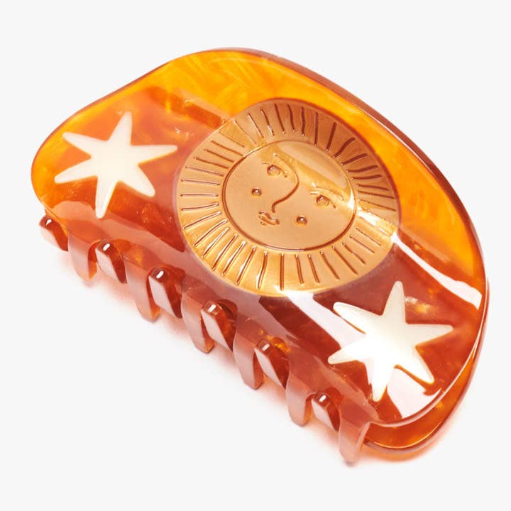 Hemera Claw by Winona Irene: an amber-colored acetate hair claw clip featuring a gold sun face emblem and white star accents.