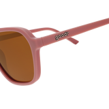 A pair of Goodr “Threaten me with a Good Time” sunglasses featuring pink frames and brown lenses, with the brand name printed on the arm.
