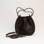Introducing the Joi Bag by Stash in Coffee—a small, dark brown leather drawstring bag with thin straps, inspired by Japanese design, displayed against a plain white background.
