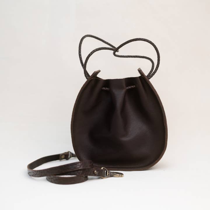 Introducing the Joi Bag by Stash in Coffee—a small, dark brown leather drawstring bag with thin straps, inspired by Japanese design, displayed against a plain white background.