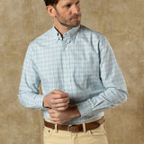 A man adjusts his left cuff while wearing the Duck Head Cotton Oxford Sport Shirt and beige pants, standing against a plain tan background.