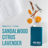 A bottle of Central Coast Laundry Detergent by Mozi is pictured alongside sliced oranges, cinnamon sticks, and sprigs of lavender on a white background. The text reads: “Smells like: Sandalwood Citrus Lavender.” A soft white towel rests in the corner, adding to the refreshing scene.