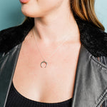 A woman wearing the Sterling Silver Crescent Moon Necklace by Ornamental Things, a black ribbed top, and a black faux fur-collared leather jacket.