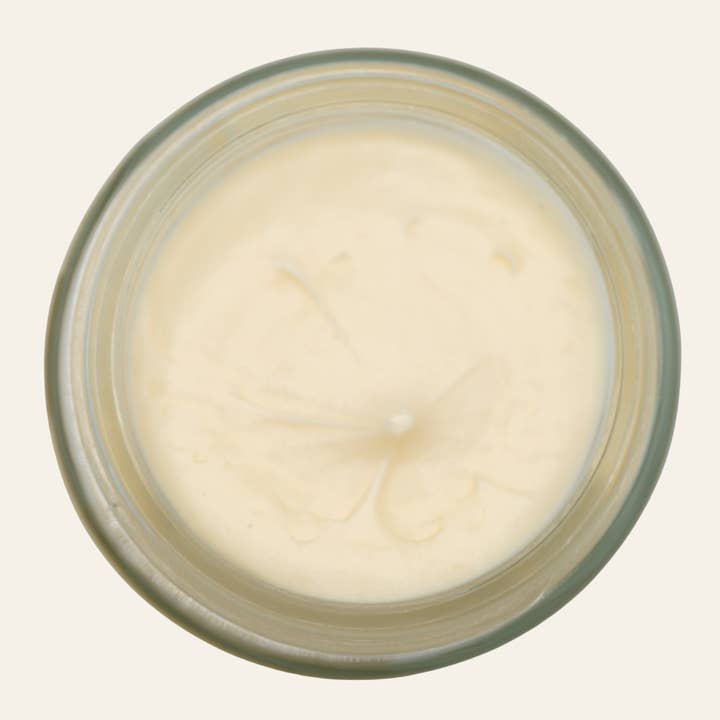Top-down view of an open glass jar filled with smooth, pale yellow Calendula Tallow Face Cream by OCASA, a moisturizer for oily combination skin.