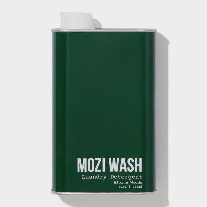 A dark green metal container labeled “Alpine Woods Laundry Detergent | Mozi” in 32oz (946ml) size, featuring a white cap on the top left, evokes fresh pine notes and subtle hints of sandalwood.