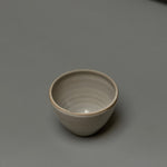 The Stoneware Smudge Bowl by Incausa, a small, round, light gray hand-thrown piece with an in-house glaze, is displayed on a smooth gray surface with minimal shadows.