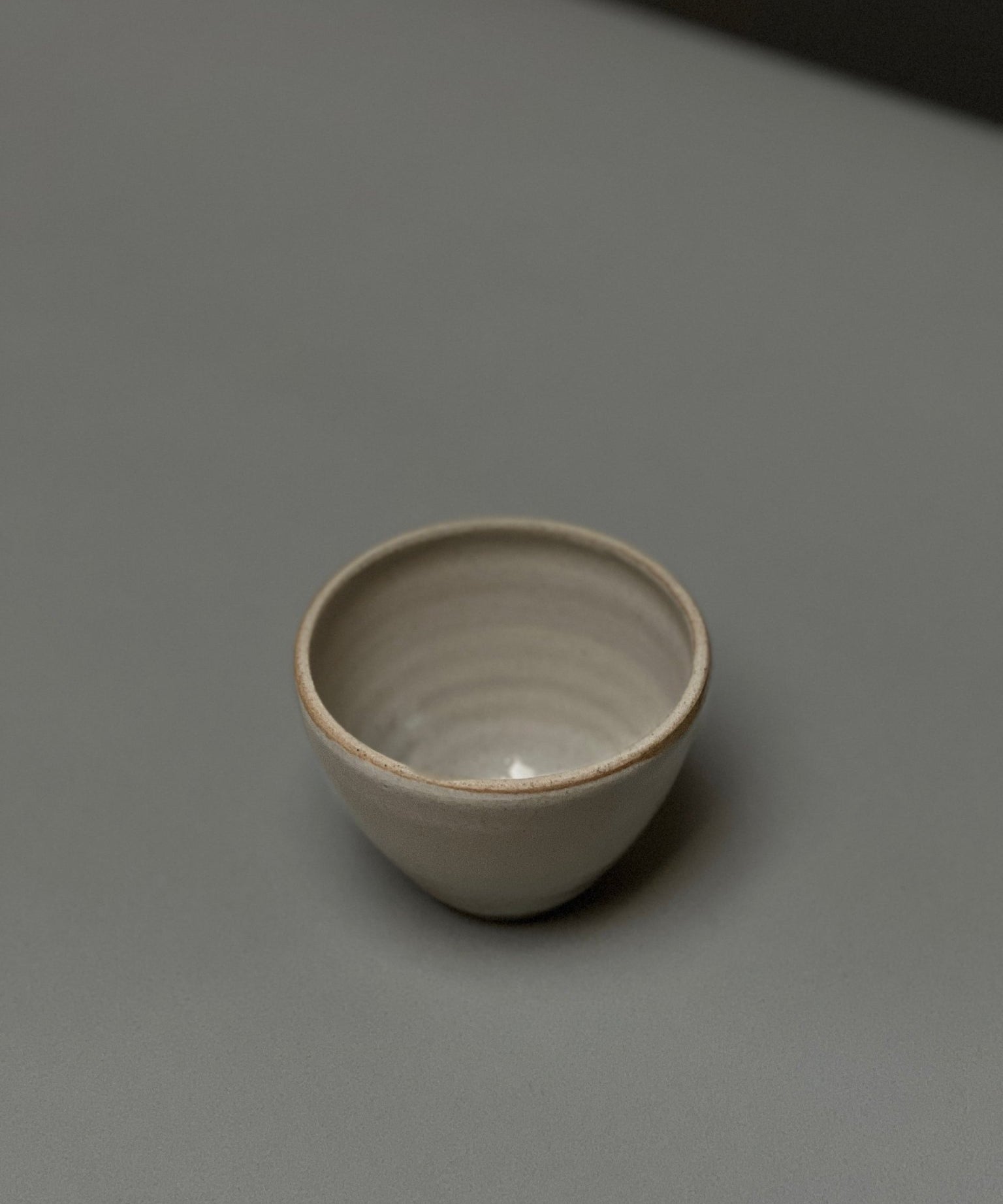 The Stoneware Smudge Bowl by Incausa, a small, round, light gray hand-thrown piece with an in-house glaze, is displayed on a smooth gray surface with minimal shadows.