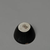 The Incausa Stoneware Smudge Bowl is shown upside down on a gray surface, displaying its beige base with a dark geometric design and in-house glaze.
