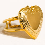 Sefina Locket Heart Ring by Flanerie by MAIQ featuring a gold heart-shaped locket with ornate filigree detailing along the border and an adjustable fit.